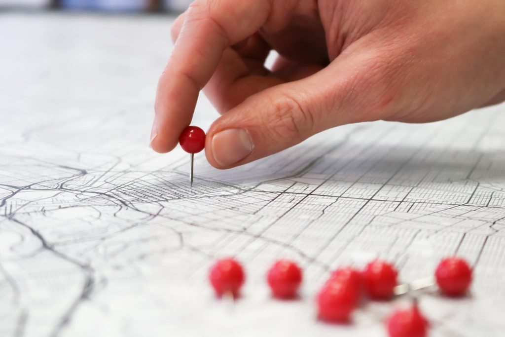 Hand plotting a red pin onto a white map