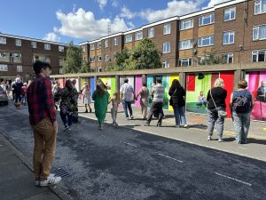 Painted garages in a housing estate, featuring the faces of people living in the area. People are looking at these garages | RUOS Evaluation Case Study