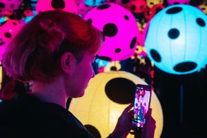 A young person taking a photograph on their mobile phone of a colourful exhibition