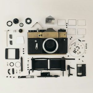 Photograph of a deconstructed analogue film camera with its parts spread across a white background