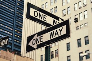 Two street signs that read: 'One Way' pointing the opposite direction of each other in front of tower blocks