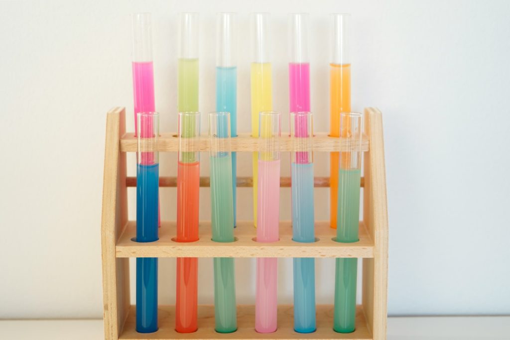 test tubes filled with different coloured liquids in a wooden rack