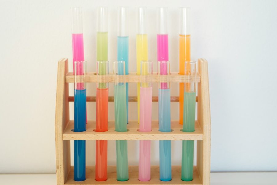 test tubes filled with different coloured liquids in a wooden rack