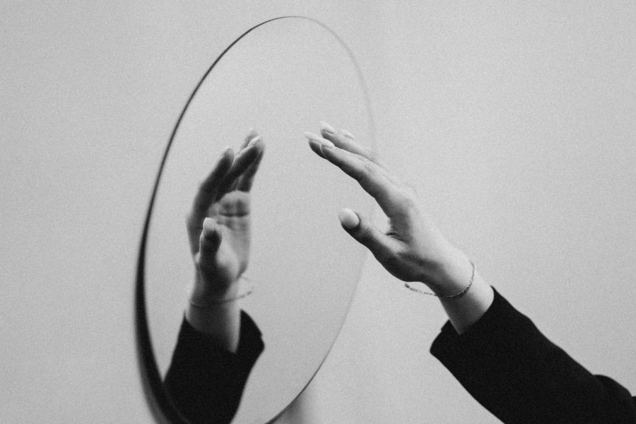 A black and white image of someone's hand reaching towards a mirror